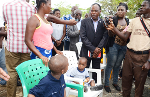 Deux jeunes enfants africains assis sur des chaises de plastique entourés d'officiels 