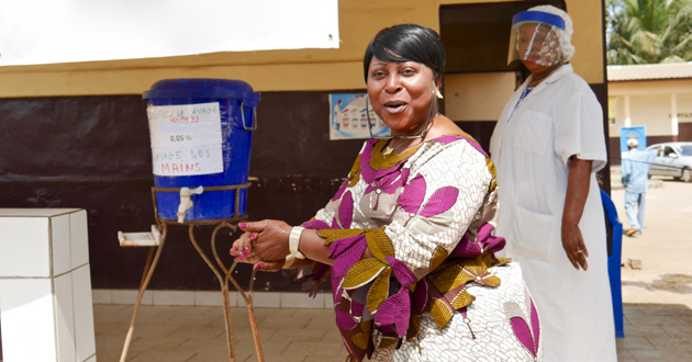 En Guinée, une femme souriante, Directrice du centre médical de Coléa se lave les mains sous un réservoir d'eau