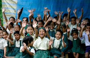 Un groupe d'enfants souriants en uniforme vert et blanc lèvent les mains