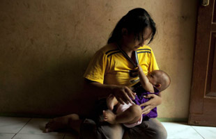 A woman breastfeeds her baby in a dark room in Jakarta, Indonesia.